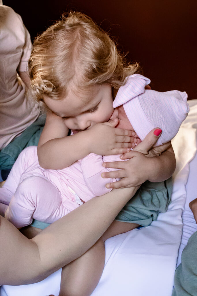 Toddler hugging and holding her new baby sister 