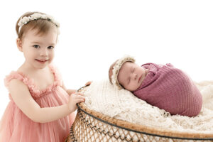 little girl smiling at cleveland photographer as she poses next to newborn at her session. 