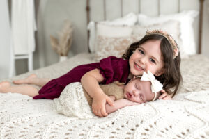 Big sister holding baby sister on bed 