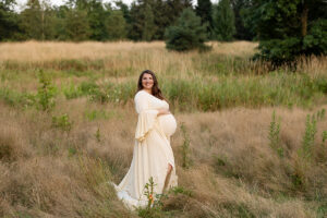 Mom holding her pregnant belly smiling at Ohio State ATI Gardens in Wooster during fall