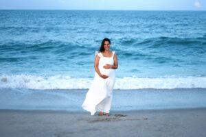 A pregnant woman standing on the beach at sunset, holding her baby bump with both hands and smiling peacefully—celebrating her IVF pregnancy with gratitude and joy.