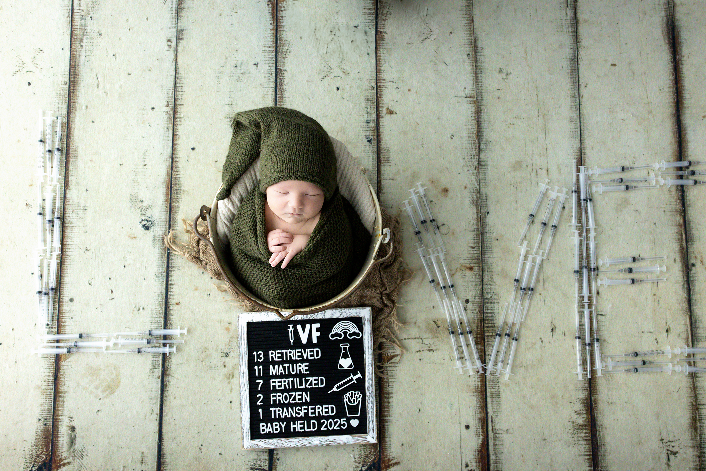 Newborn baby in a bucket surrounded by IVF needles spelling the word “love” — symbolizing an IVF journey and miracle baby