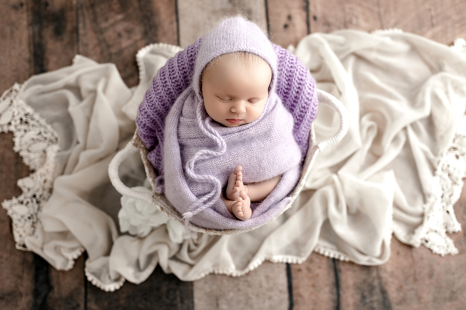 Newborn baby girl at her cleveland photo session snuggled in soft purples and ivory lace backdrop