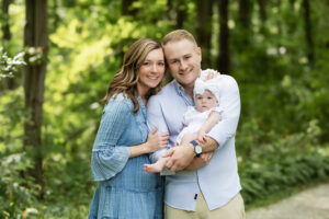 New parents lovingly holding their infant during a golden hour extended family photo shoot in a peaceful park.