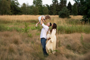 Family wearing neutral colors laughing and playing together in a high grass field in the fall. 