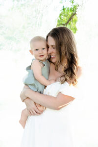 mom snuggling baby outside by a clothes line holding beautiful lace. baby looks at the camera knowing how loved he is. 