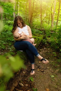mom breastfeeding daughter on a fallen tree in the woods with the sun radiating down on them softly