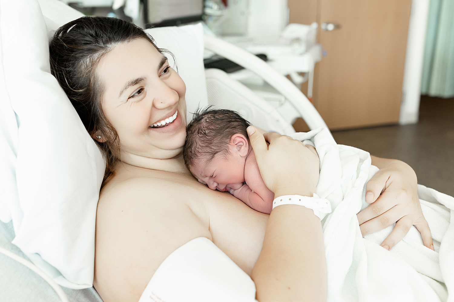 Mom smiling at husband while snuggling her fresh newborn after her delivery