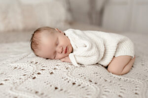 baby snuggled on bed wearing a thick knit romper 