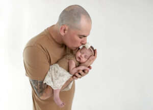 Dad leaning in and kissing newborn on her head tenderly at their newborn photo session in cleveland