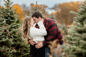 couple embrased closely cuddling in, smiling at each other at Gale House tree farm for their photo session
