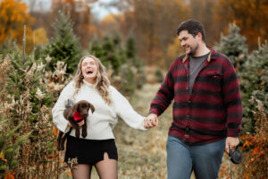 Couple smiling at Galehouse Tree Farm with their two dogs during a Christmas mini session in Northeast Ohio.