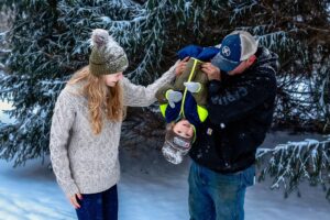 family playing in snow together at medina park. little boy is laughing as day holds him upside down, playingly.