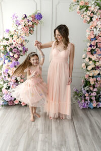 Mother and daughter laughing and dancing together on soft neutral backdrop during Mother’s Day mini session